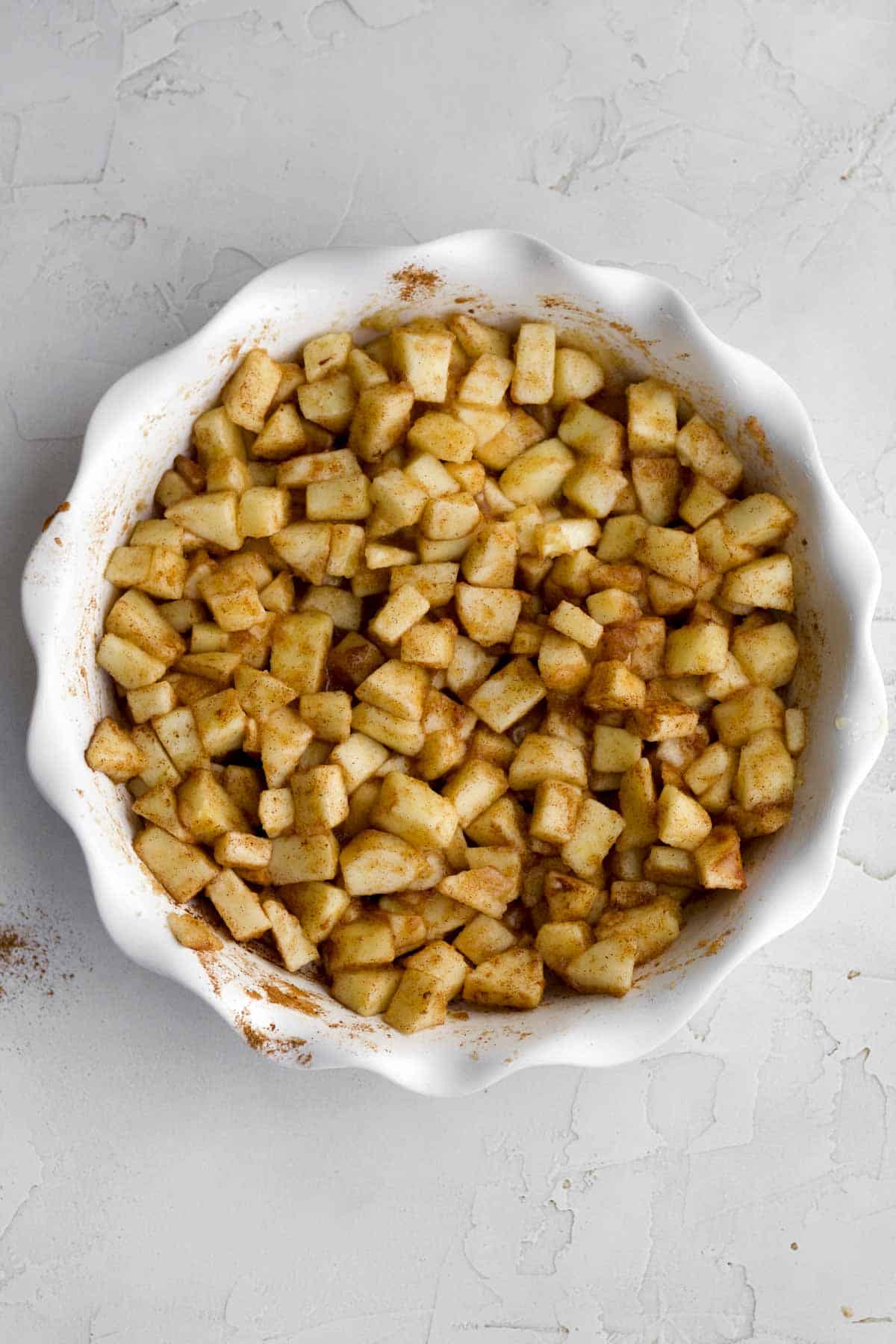 A baking dish with chopped apples, cinnamon and applesauce mixed together.